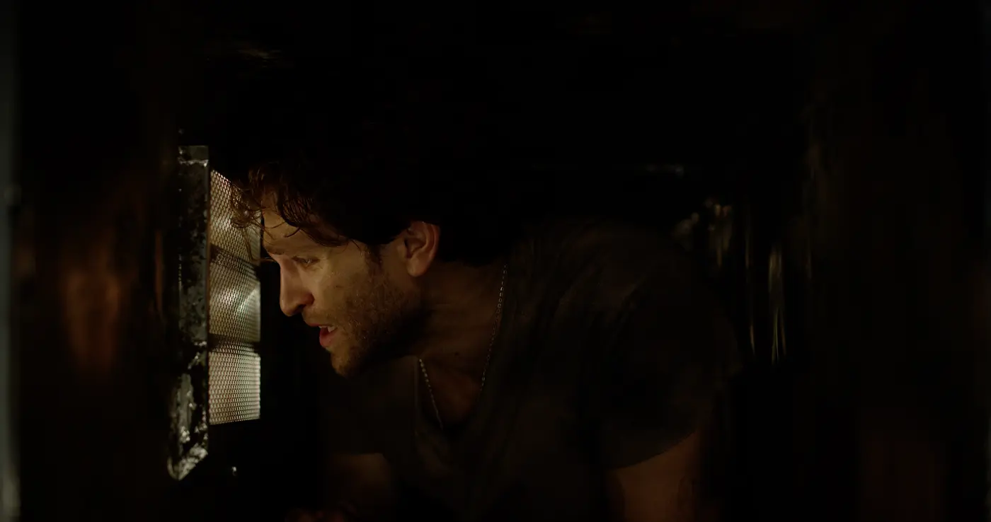 Cole crawls through a dark ventilation shaft while trying to escape in No Escape 2020
