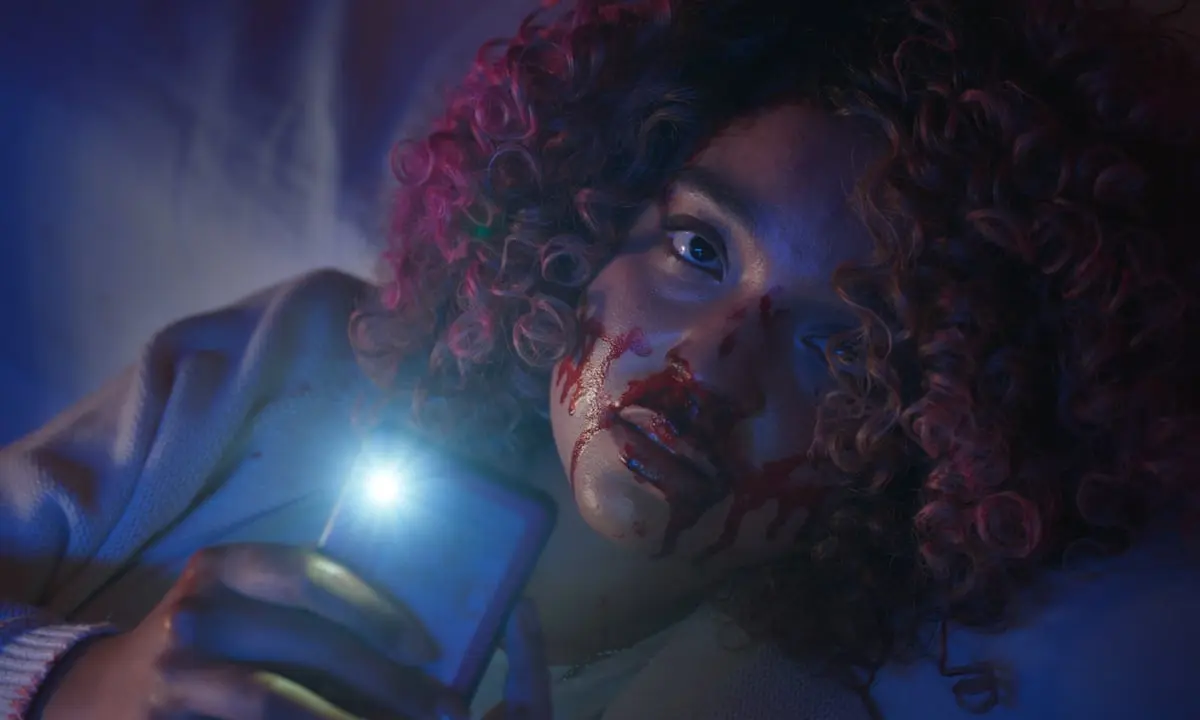 A bloodied Cecilia holds her phone while creating her false survivor story in Sissy 2022