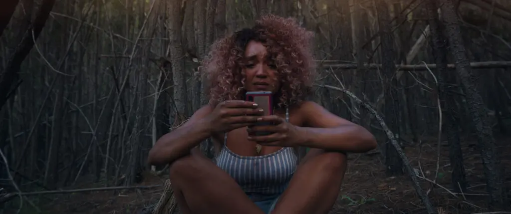 Cecilia sits alone in the woods checking her phone in Sissy 2022